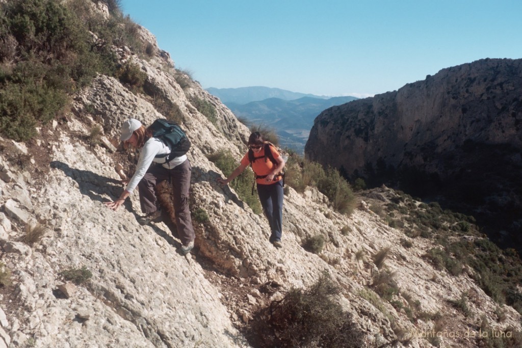 Asun y la hermana de Mónica subiendo a la Penya Migjorn por pasos de roca, al fondo queda la Sierra de La Grana y detrás más alta Aitana